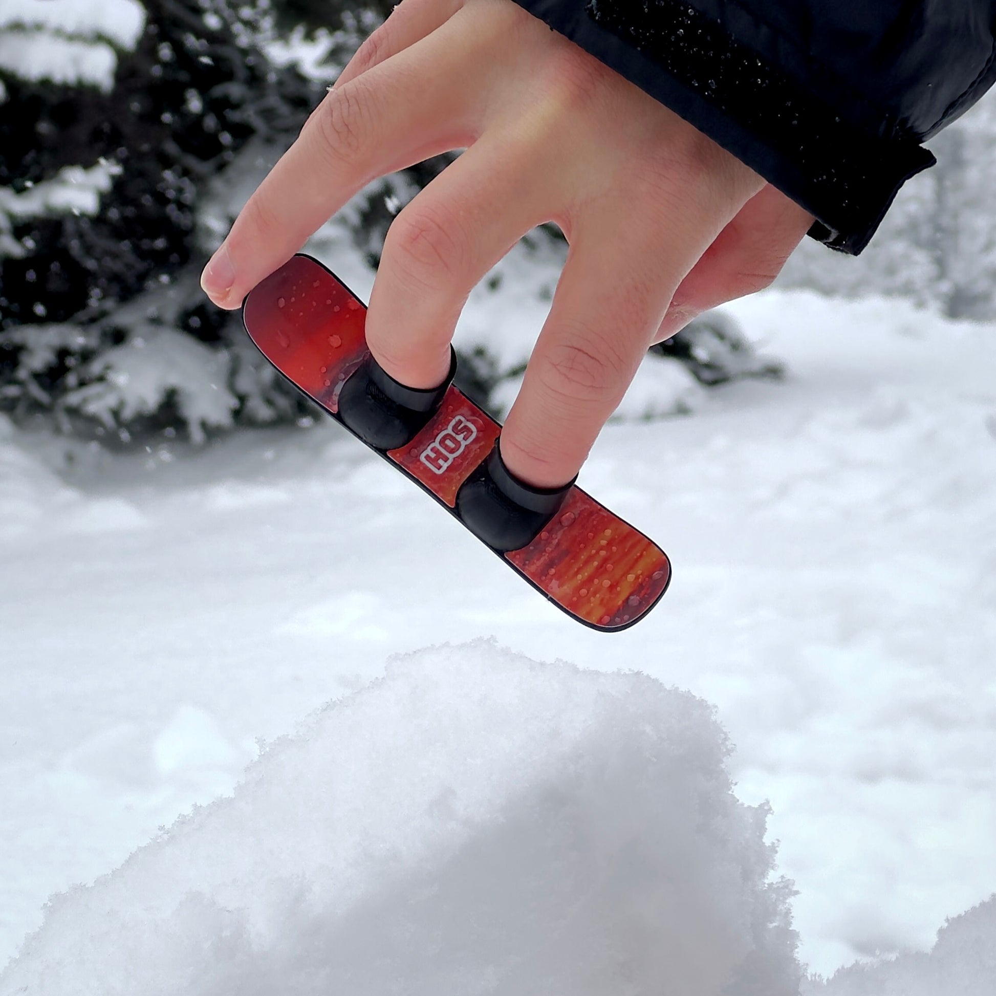 Jumping SlideofHand Finger Snowboard black with red sunrise graphic in snow